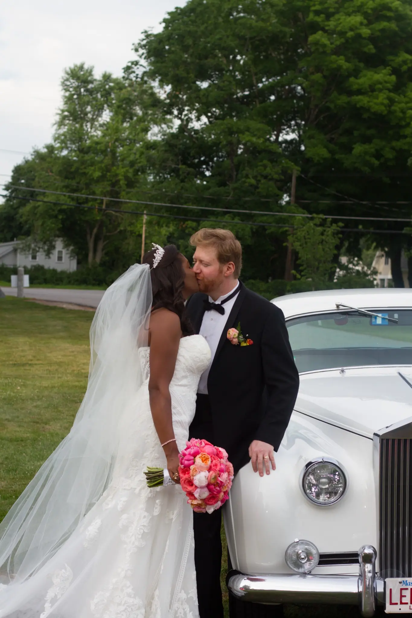 Bride and groom kissing beside a vintage white car